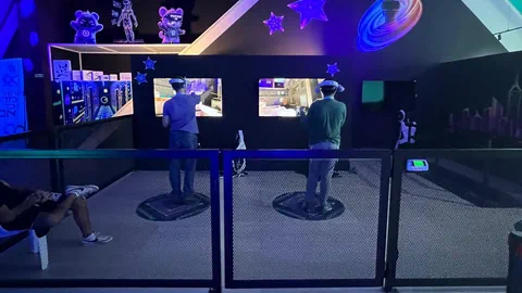 Two adult players side by side at the standing VR stations