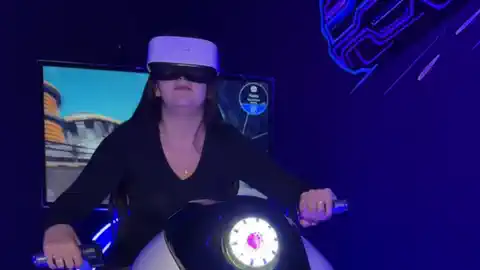 A woman riding the motorcycle simulator in a VR headset