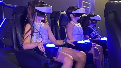 שלוש בנות עם משקפי VR ובקרים בשורת כיסאות התנועה